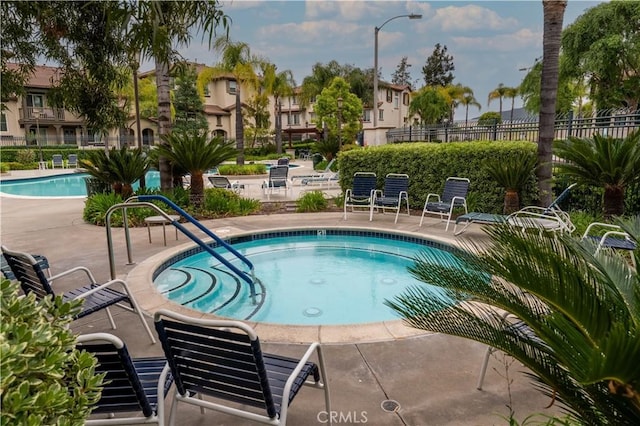 community pool with fence, a community hot tub, and a patio