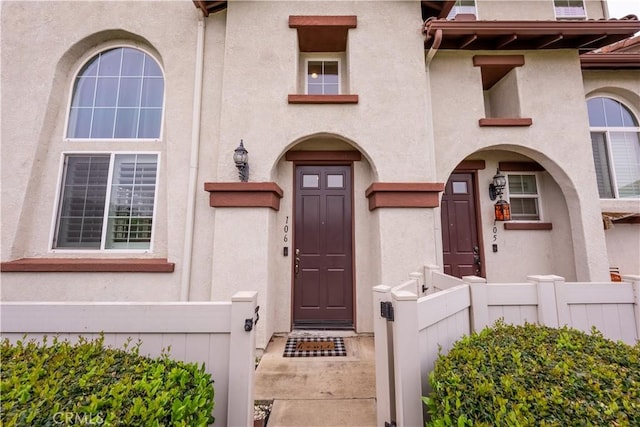 view of exterior entry with stucco siding and fence