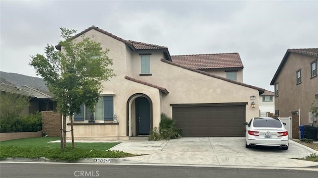 mediterranean / spanish-style house featuring a front yard, an attached garage, a tile roof, concrete driveway, and stucco siding