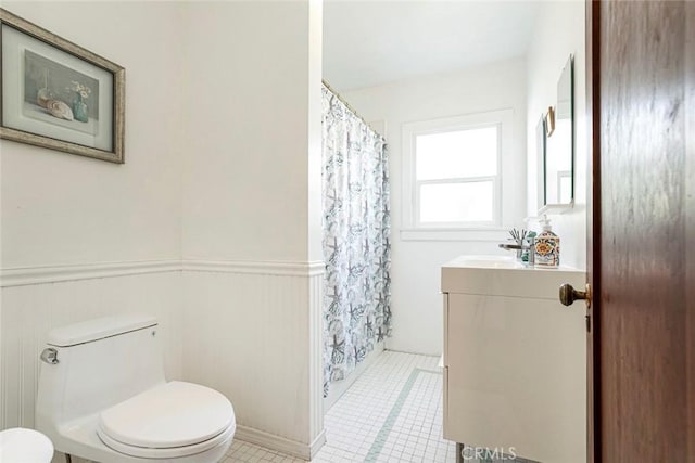 full bath featuring tile patterned floors, toilet, vanity, and a wainscoted wall
