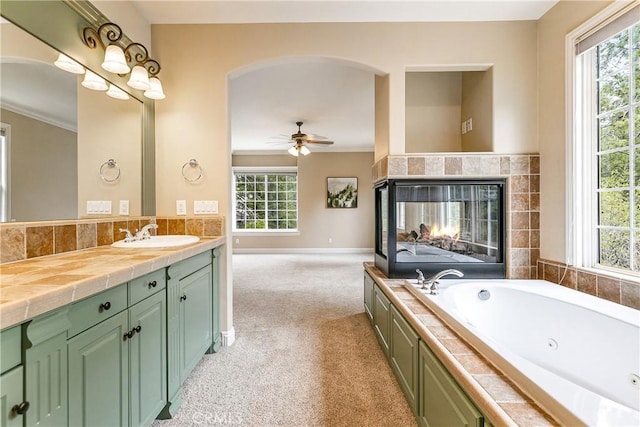 bathroom with a multi sided fireplace, vanity, ornamental molding, a ceiling fan, and a whirlpool tub