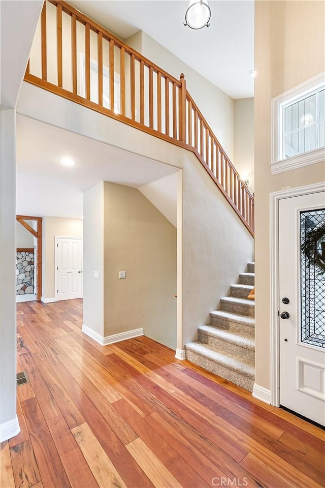 foyer featuring baseboards, wood-type flooring, visible vents, and stairway