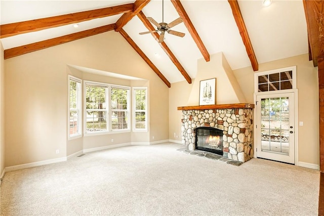 unfurnished living room featuring ceiling fan, beam ceiling, a stone fireplace, and carpet floors