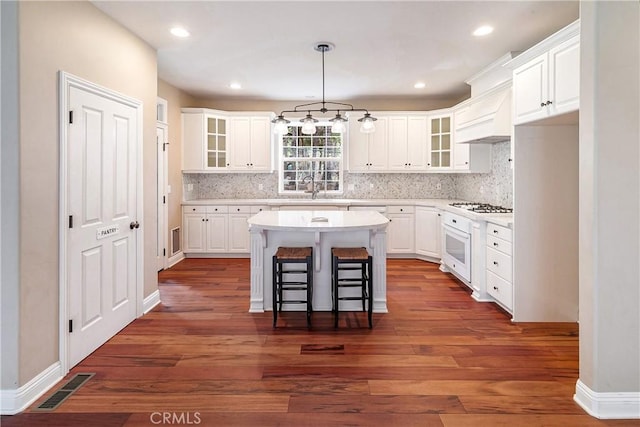 kitchen featuring white appliances, white cabinets, visible vents, a breakfast bar, and a sink