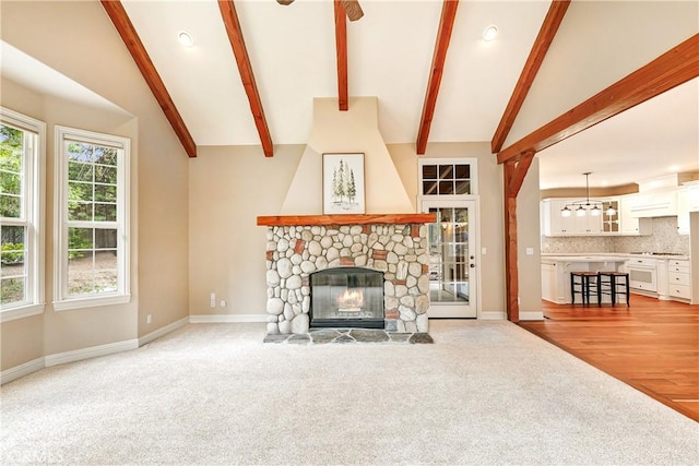 unfurnished living room featuring baseboards, light colored carpet, lofted ceiling with beams, and a stone fireplace