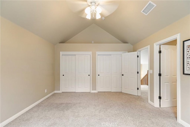 unfurnished bedroom featuring multiple closets, visible vents, vaulted ceiling, and light colored carpet