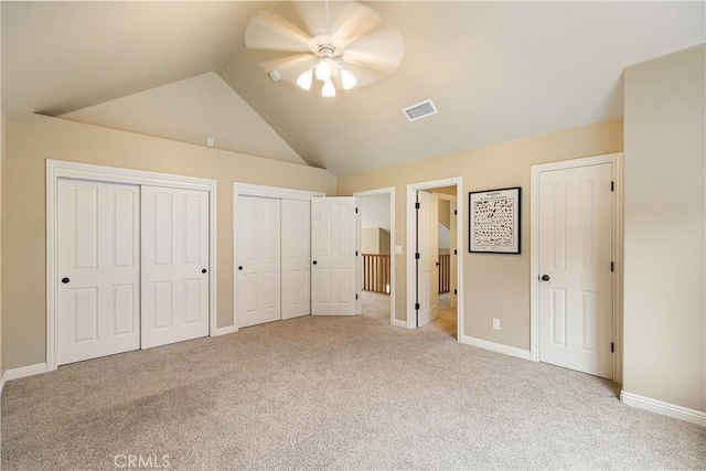 unfurnished bedroom with multiple closets, light carpet, baseboards, lofted ceiling, and visible vents