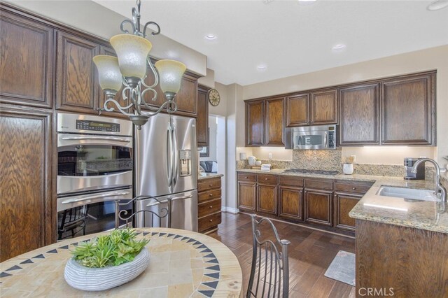 kitchen with dark wood-style flooring, light stone counters, a chandelier, stainless steel appliances, and a sink