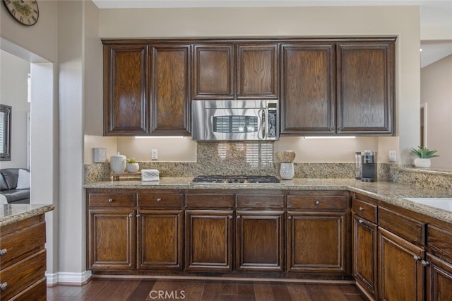 kitchen with dark brown cabinetry, light stone counters, backsplash, dark wood finished floors, and stainless steel appliances