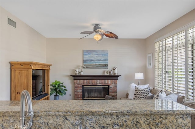 living room featuring visible vents, a ceiling fan, and a brick fireplace