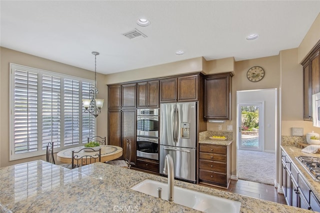 kitchen featuring dark brown cabinets, visible vents, wood finished floors, a sink, and stainless steel appliances