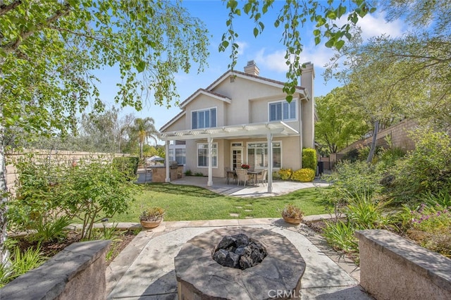rear view of house with a yard, stucco siding, a patio, a fire pit, and a chimney