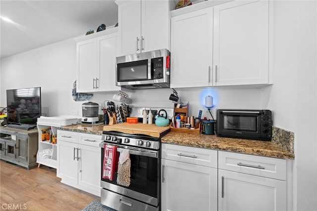 kitchen with appliances with stainless steel finishes, a toaster, white cabinets, stone counters, and light wood-style flooring