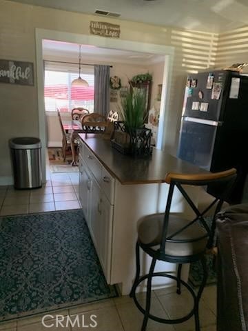 kitchen featuring visible vents, white cabinets, light tile patterned floors, dark countertops, and a kitchen breakfast bar