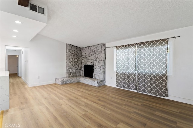 57526 Onaga, Yucca Valley, CA 92284 - unfurnished living room with visible vents, baseboards, a stone fireplace, a textured ceiling, and wood finished floors