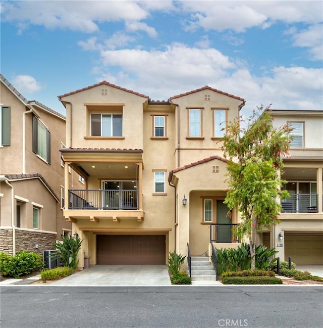 view of front facade with a tiled roof, a balcony, stucco siding, driveway, and a garage