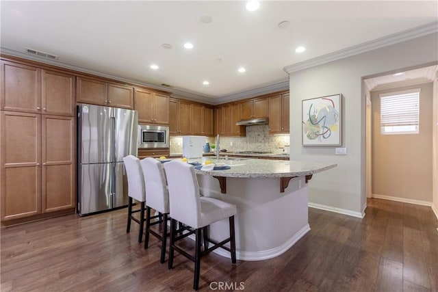 kitchen with under cabinet range hood, stainless steel appliances, a breakfast bar, visible vents, and decorative backsplash