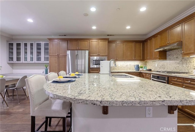kitchen featuring crown molding, a sink, a breakfast bar area, stainless steel appliances, and under cabinet range hood