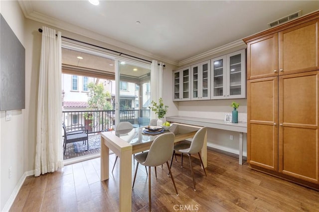 dining area featuring baseboards, light wood-style flooring, visible vents, and ornamental molding