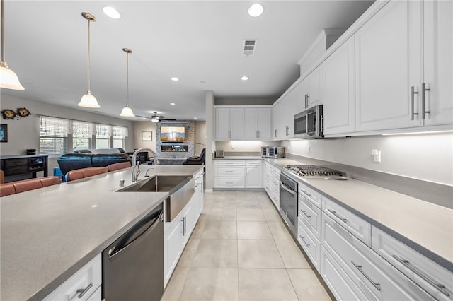 kitchen with a sink, open floor plan, light tile patterned flooring, white cabinets, and appliances with stainless steel finishes
