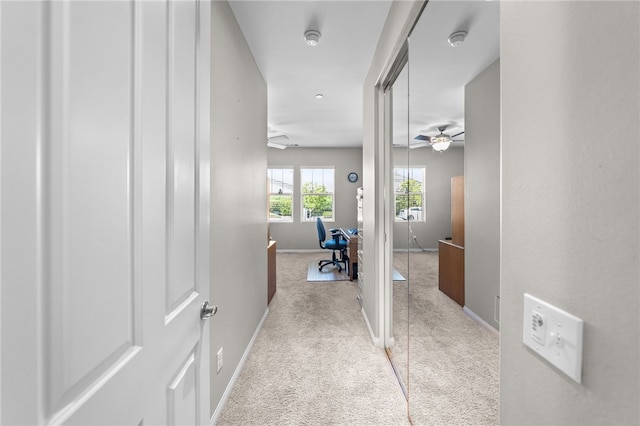 corridor featuring light colored carpet and baseboards