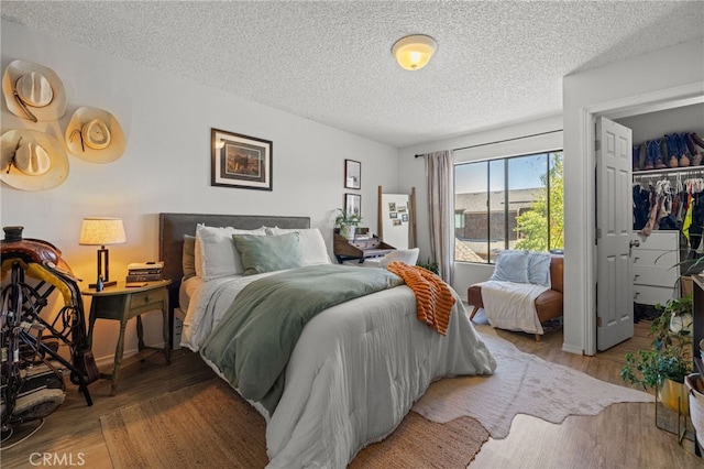 bedroom with a walk in closet, a textured ceiling, and wood finished floors