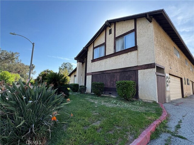 2453 S Ridgewood Dr, West Covina, CA 91792 - view of side of property with stucco siding, a lawn, asphalt driveway, and a garage