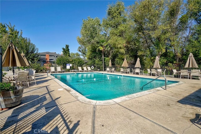 community pool with a patio area, fence, and outdoor dining space