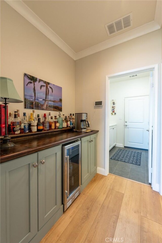 bar with a bar, light wood-style flooring, ornamental molding, wine cooler, and visible vents