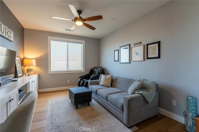 living room featuring baseboards, a ceiling fan, visible vents, and light wood-style floors