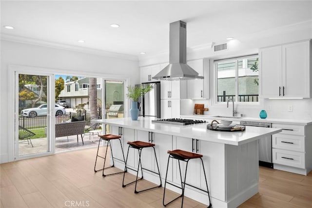 kitchen featuring a breakfast bar, island exhaust hood, visible vents, appliances with stainless steel finishes, and a sink