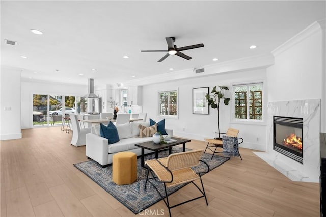 living room with a fireplace, visible vents, a ceiling fan, and crown molding