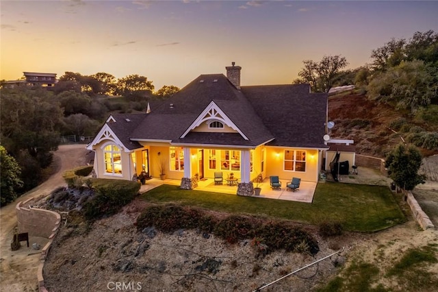 back of property at dusk featuring a patio, a chimney, fence, and a lawn