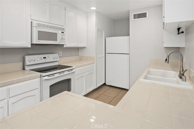 kitchen featuring tile countertops, visible vents, a sink, white appliances, and white cabinetry