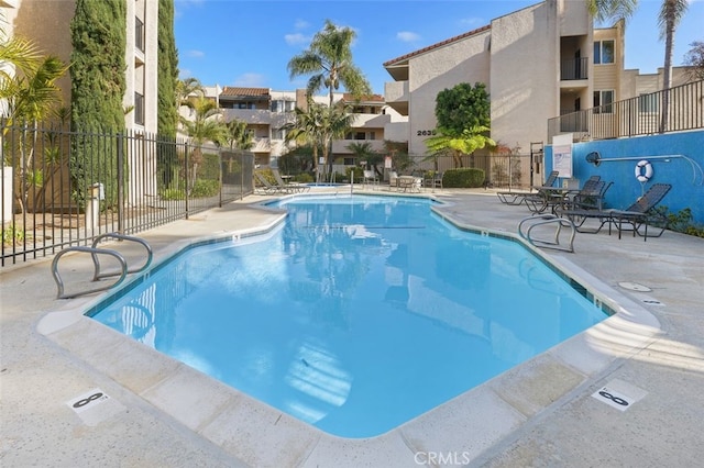 community pool with a patio area, fence, and a residential view