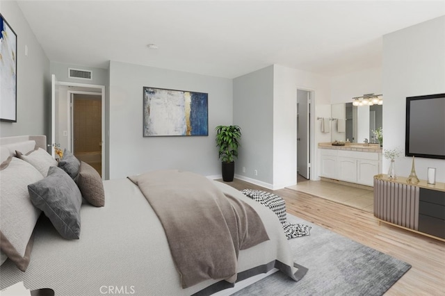 bedroom with visible vents, light wood-type flooring, a sink, baseboards, and ensuite bathroom