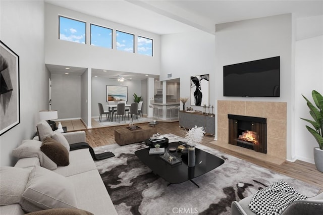 living area with ceiling fan, visible vents, a towering ceiling, a fireplace, and wood finished floors