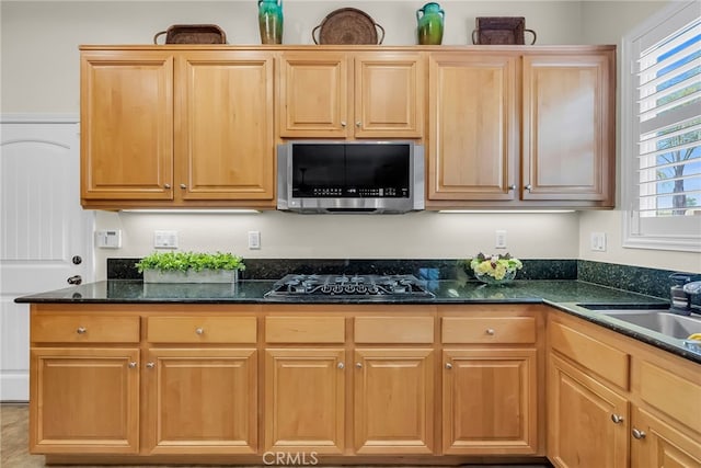 kitchen featuring stainless steel microwave, black gas cooktop, a sink, and dark stone countertops