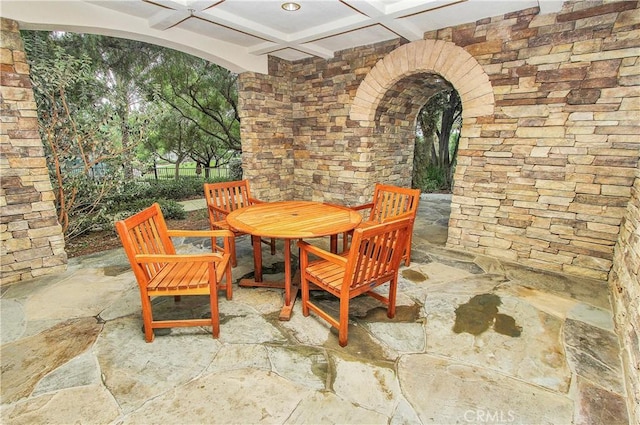 dining space featuring coffered ceiling, arched walkways, beamed ceiling, and stone floors