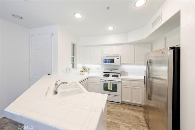 kitchen featuring visible vents, white appliances, light wood-style floors, a peninsula, and tile countertops