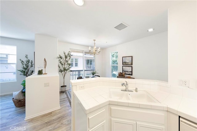 kitchen with light wood-type flooring, a chandelier, visible vents, tile countertops, and a sink