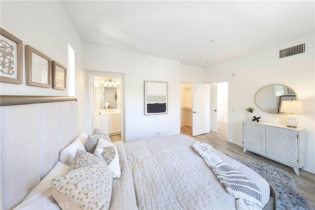 bedroom featuring baseboards, ensuite bathroom, a walk in closet, visible vents, and wood finished floors