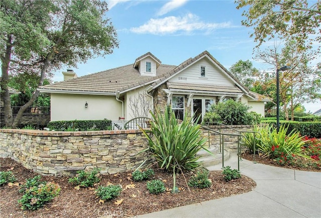 bungalow-style house with stucco siding, a tiled roof, and a chimney