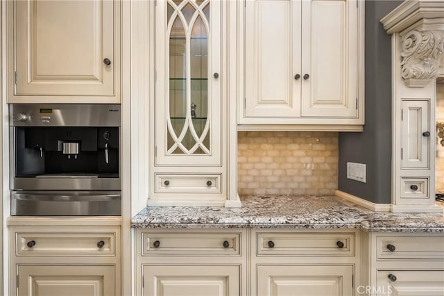 kitchen with a warming drawer, cream cabinets, light stone countertops, and glass insert cabinets