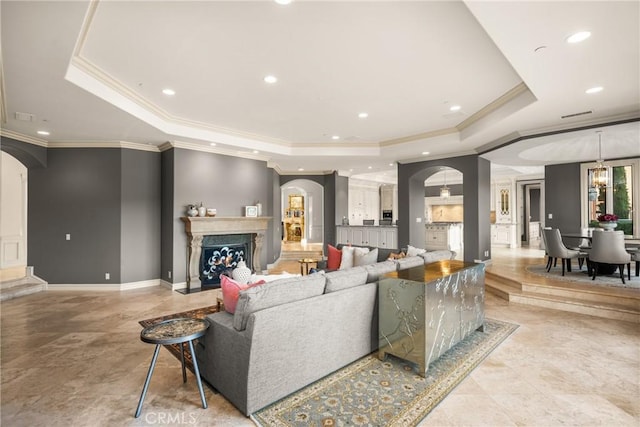 living room with baseboards, arched walkways, crown molding, and a tray ceiling