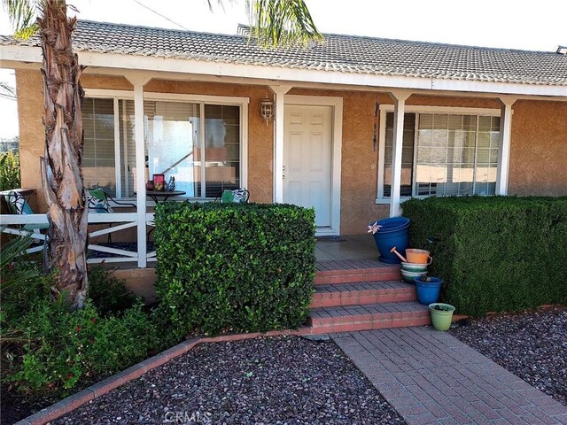 property entrance with a tiled roof, a porch, and stucco siding