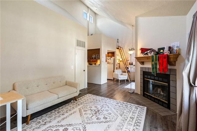 living room featuring a tile fireplace, visible vents, high vaulted ceiling, and wood finished floors