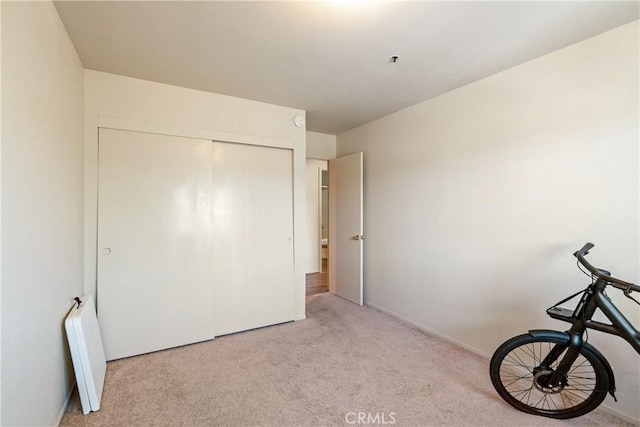 unfurnished bedroom featuring radiator, baseboards, a closet, and light colored carpet