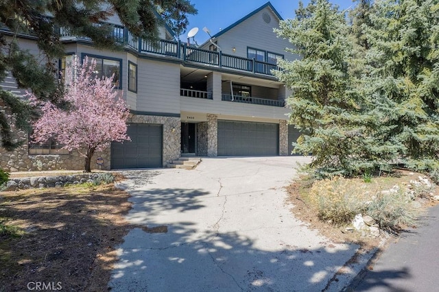 view of front of home featuring an attached garage, driveway, stone siding, and a balcony