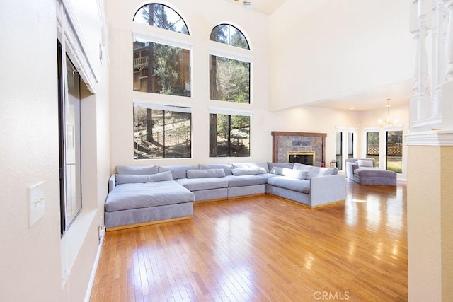 living room featuring light wood-style floors, a glass covered fireplace, a high ceiling, and an inviting chandelier